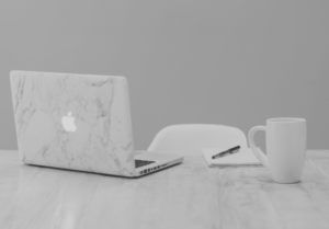 A marble-effect laptop on top of a table with a notepad and coffee cup.
